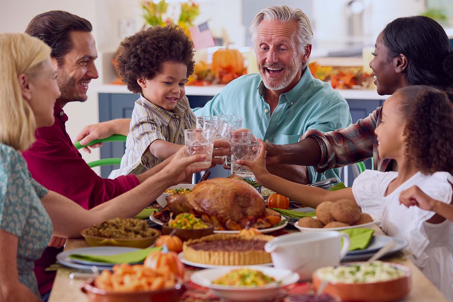 Smiling multi-generational family raising glasses around a Thanksgiving dinner table